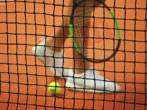 person wearing pair of white low-top sneakers while holding Wilson tennis racket