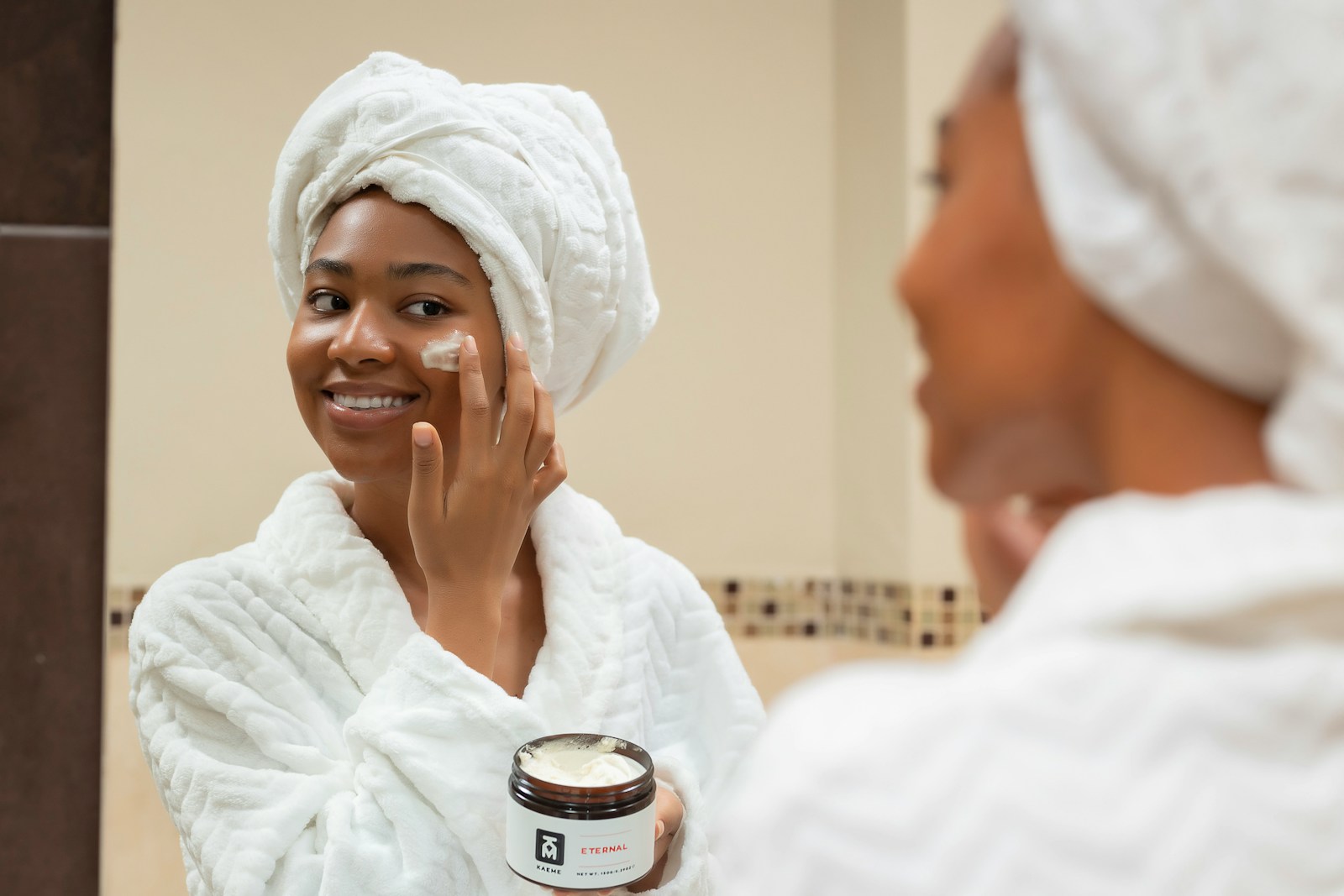 a woman with a towel on her head and a jar of cream on her face