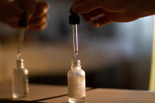 Een flesje nagelolie met pipet naast verzorgde handen met goed onderhouden nagels