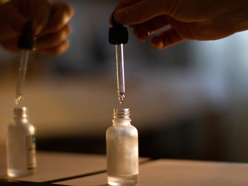 Een flesje nagelolie met pipet naast verzorgde handen met goed onderhouden nagels