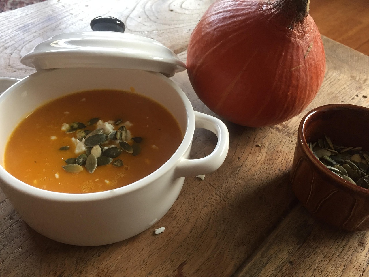 Een dampende kom pompoensoep op een houten tafel in een herfstse sfeer